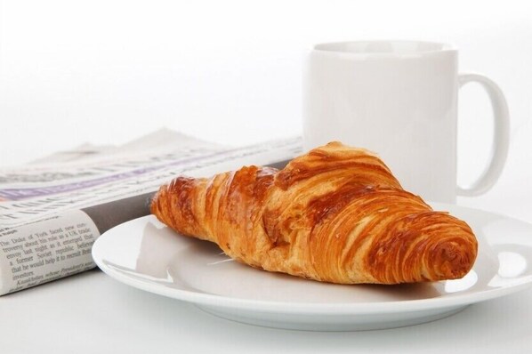 A croissant on a white plate with a white mug in the background. - Le Caldéro (Montpon-Menesterol)