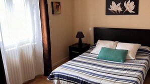 Een slaapkamer met een bed, nachtkastje, lamp en een raam met gordijnen.