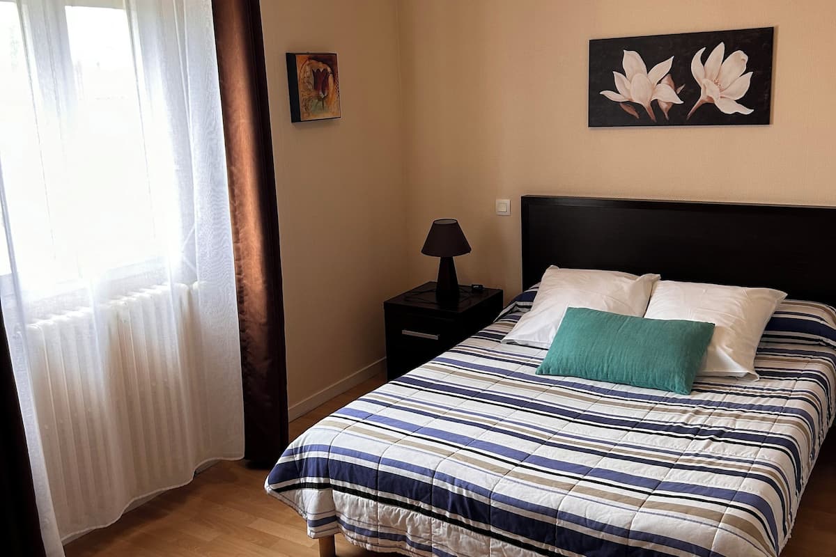 Un dormitorio con cama, mesita de noche, lámpara y ventana con cortinas.