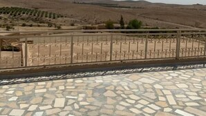 A paved terrace with a patterned floor, a metal railing, and a view of a dry, hilly landscape in the background. - Les dunes de Guemassa (Gmassa)