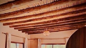 A room with a bed, two wicker sofas, a round wicker table, and a window with curtains. - Les dunes de Guemassa (Gmassa)