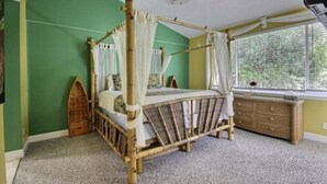 Ein Himmelsbett mit Holzrahmen und weißer Bettwäsche, eine Holzkommode und ein Fenster mit Jalousien.