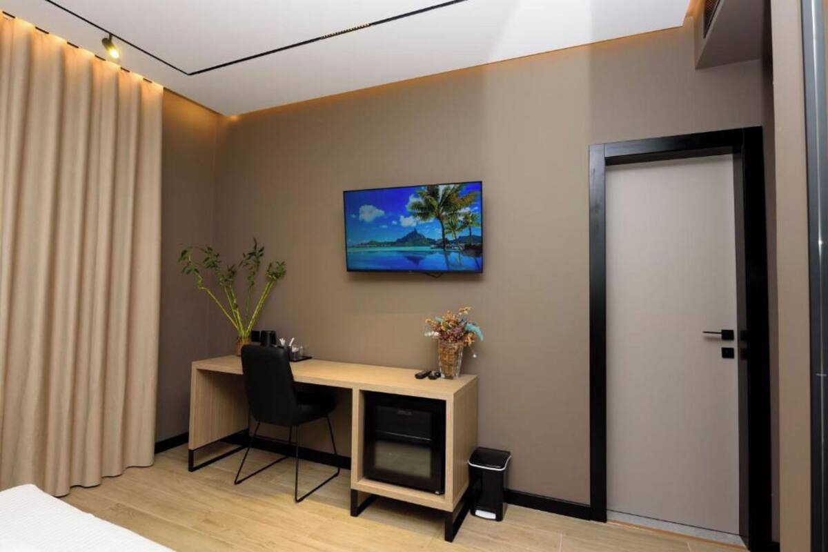 A modern hotel room with a desk, chair, and a painting of a tropical beach.