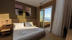 A modern hotel room with a large bed, a desk, and a balcony with a view. - Perla Del Sol (Vlorë)
