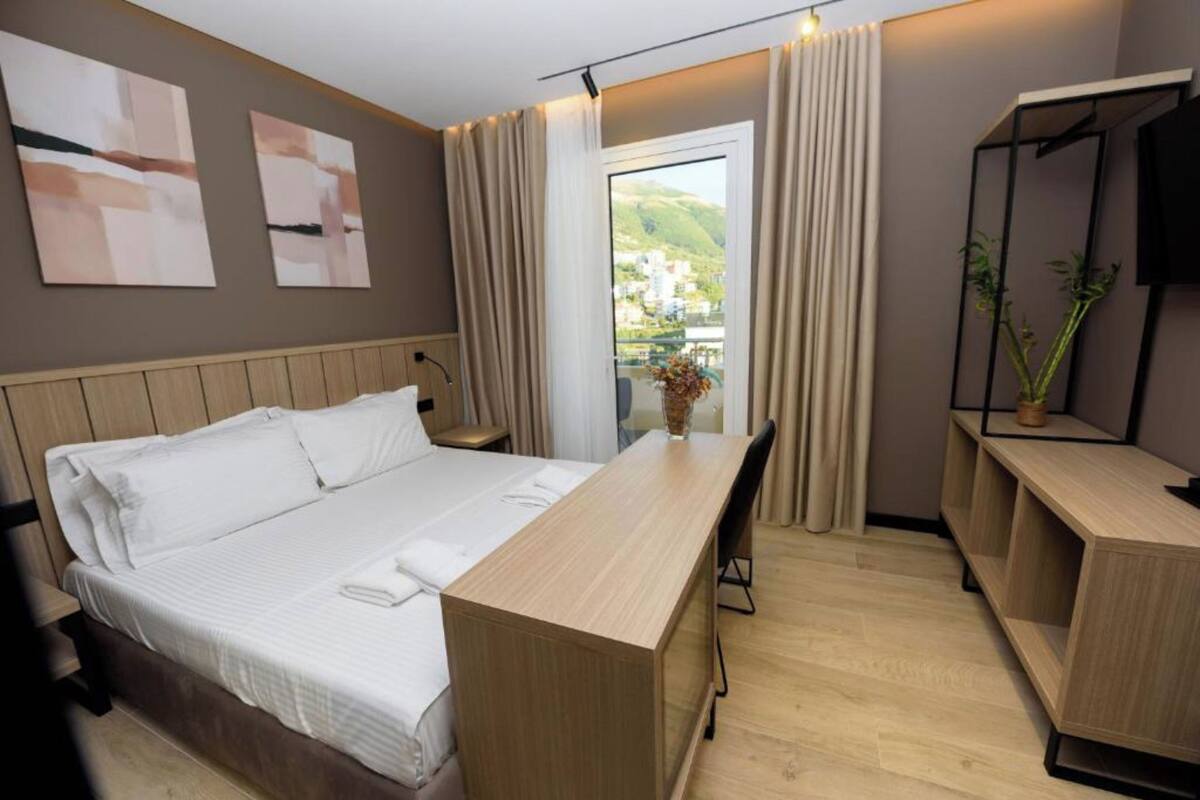 A modern hotel room with a bed, a desk, and a view of the outdoors.
