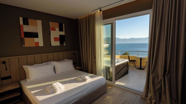 A hotel room with a bed, a view of the sea, and a balcony with a table and chairs. - Perla Del Sol (Vlorë)