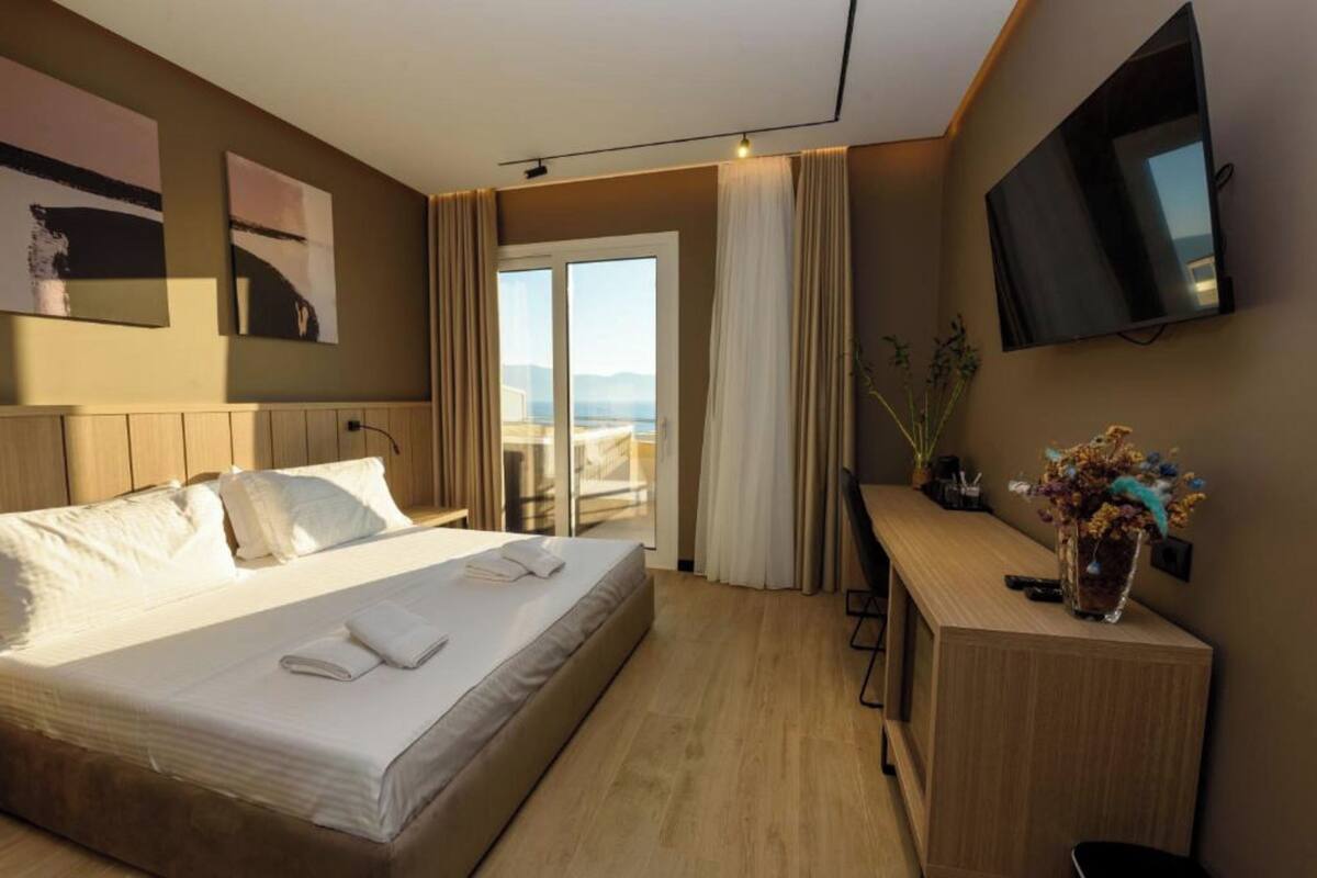 A hotel room with a bed, a desk, a TV, and a view of the outdoors.