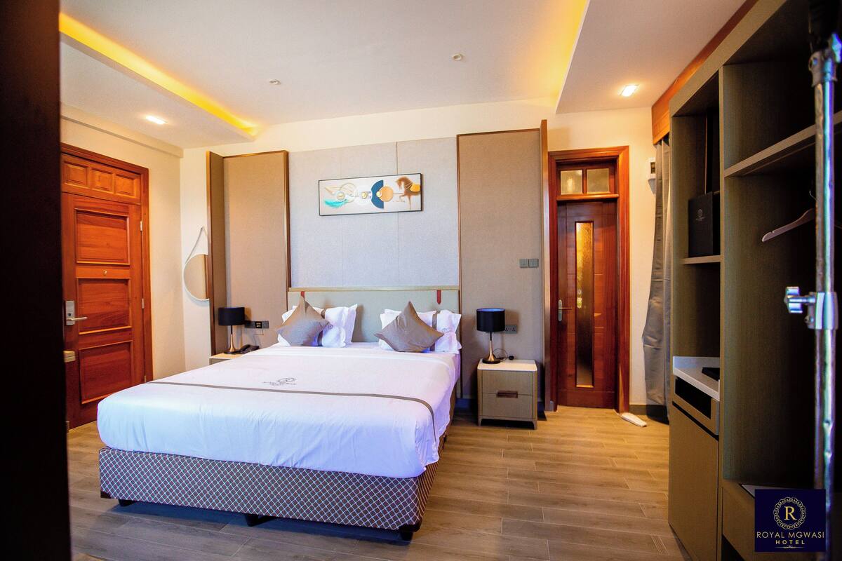 Quarto de hotel com uma cama grande, mesas de cabeceira, um guarda-roupa e um quadro na parede.