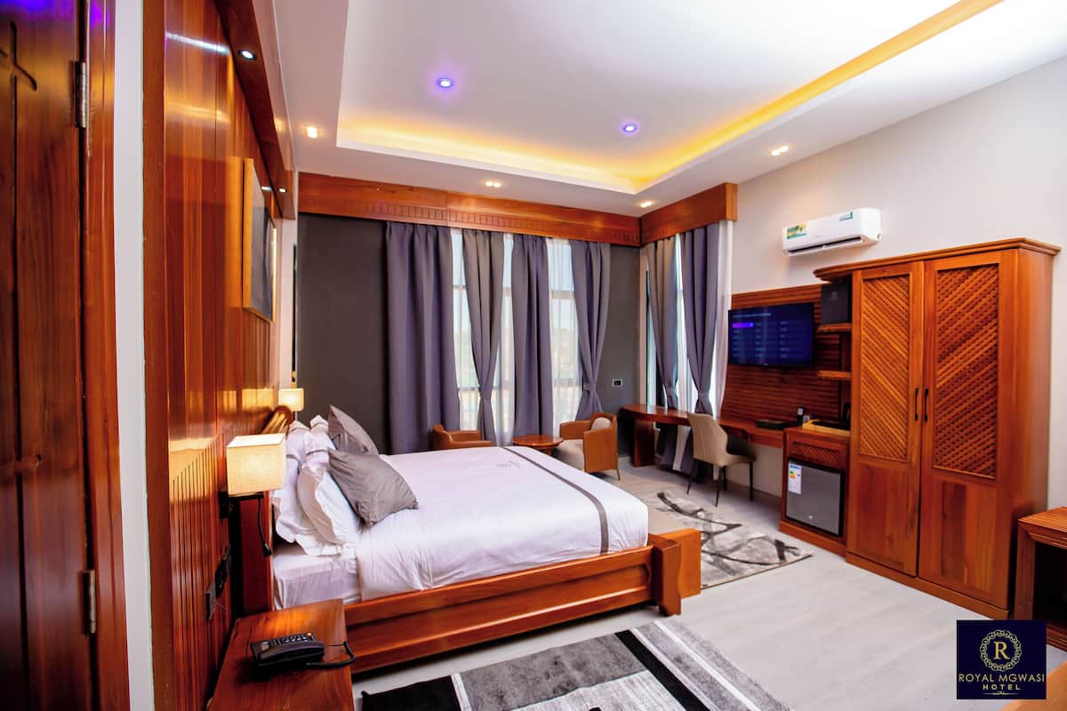 Quarto de hotel com cama grande, escrivaninha, televisão e guarda-roupa.