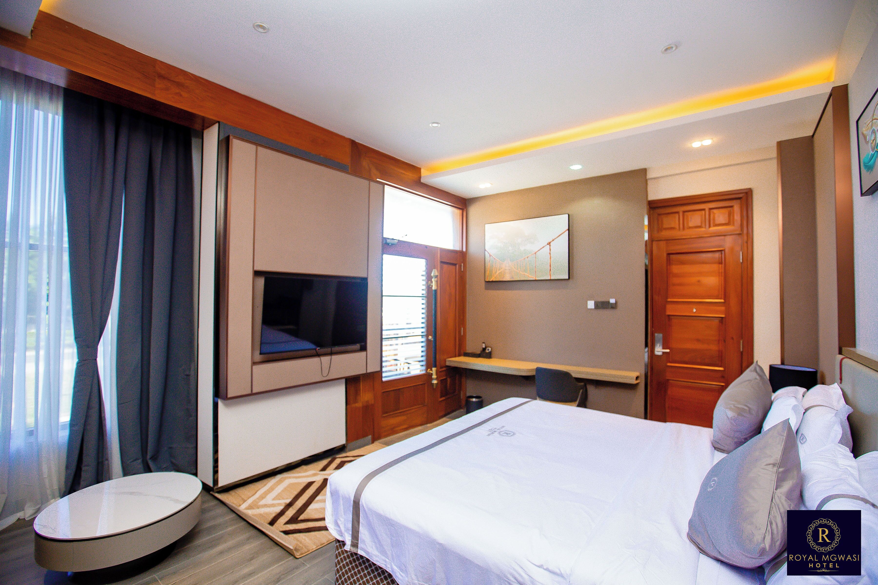 A hotel room with a bed, a TV mounted on the wall, a desk, and a door.