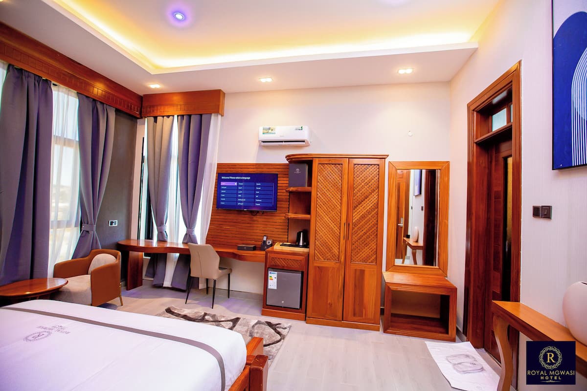 Quarto de hotel com cama, escrivaninha, cadeira, guarda-roupa e televisão.