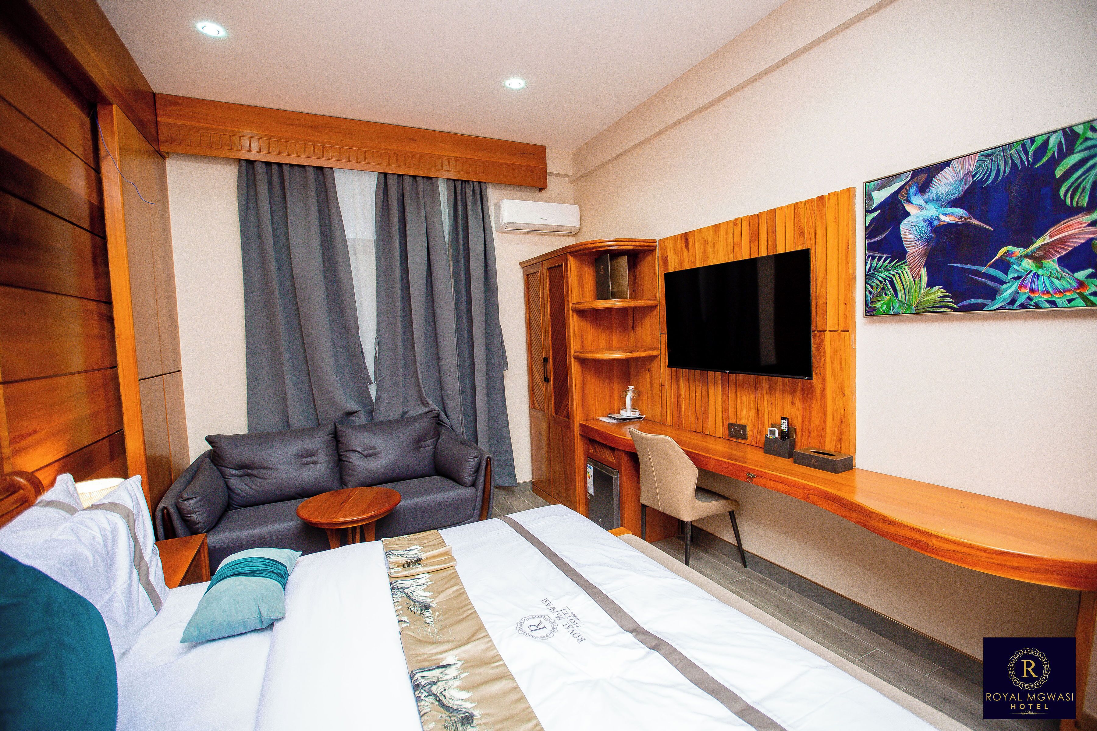 A hotel room with a bed, a sofa, a desk, and a TV mounted on the wall.