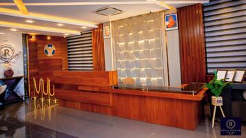 A hotel reception area with a wooden reception desk, a wall-mounted photo, and a potted plant.