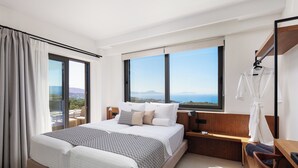 A modern hotel room with a large bed, a nightstand, a wooden bench, and a view of the sea.