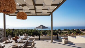 An outdoor dining area with a table set for four, overlooking a scenic view of the sea and greenery.