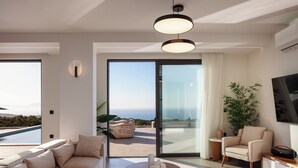 A modern living room with a sofa, a coffee table, a chair, and a large window offering a view of the sea.