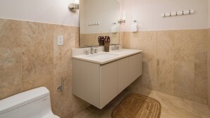 Un baño moderno con un lavamanos blanco, un espejo grande y baldosas color beige.