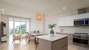 Una cocina moderna con una isla central, un comedor con mesa y sillas, y vistas al exterior a través de grandes ventanales.