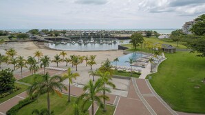 Marina con barcos, piscina y zona de playa con palmeras.