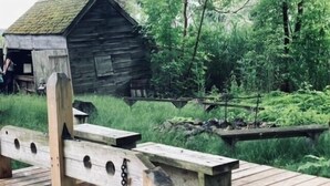 A rustic wooden structure with a sloped roof, a wooden bench with holes, and a chain attached to a wooden post. - In home mini wing private space. 💜Stay at Hal's Salem, MA (Salem)