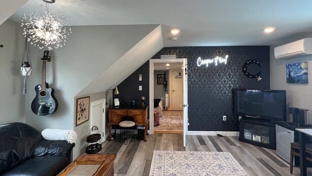 A modern living room with a black leather sofa, a wooden coffee table, a TV, and a chandelier. - In home mini wing private space. 💜Stay at Hal's Salem, MA (Salem)
