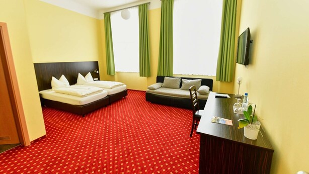 A hotel room with two beds, a sofa, a desk, and a TV.