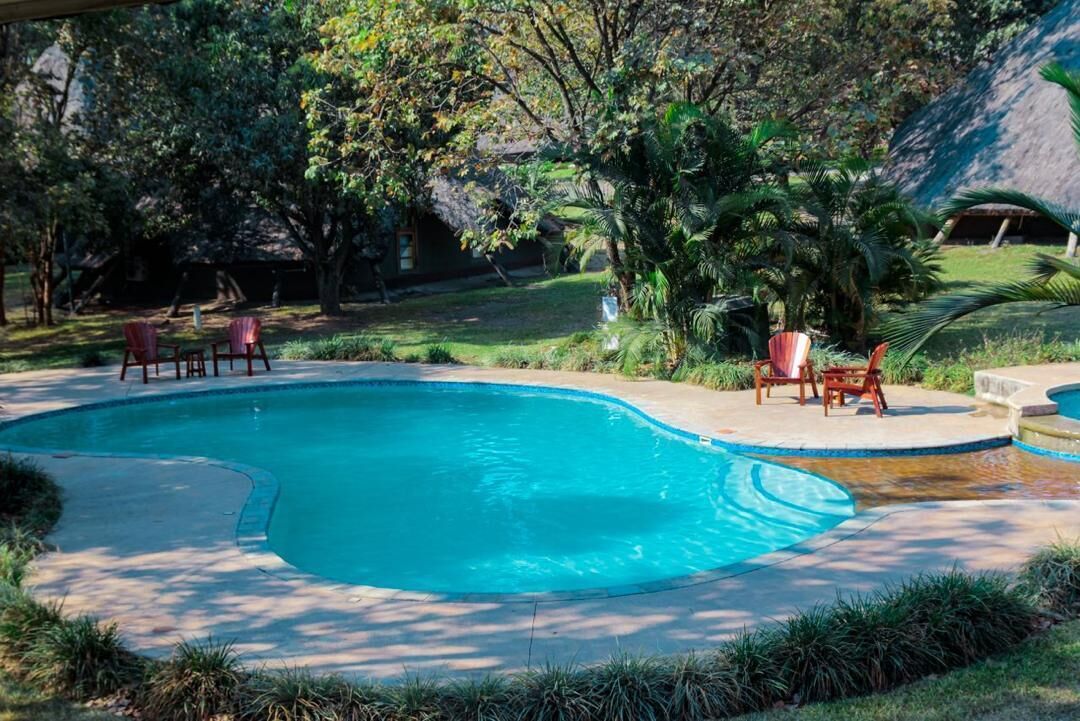 A swimming pool with a curved edge, surrounded by a concrete deck. There are two red chairs and a single red lounge chair.