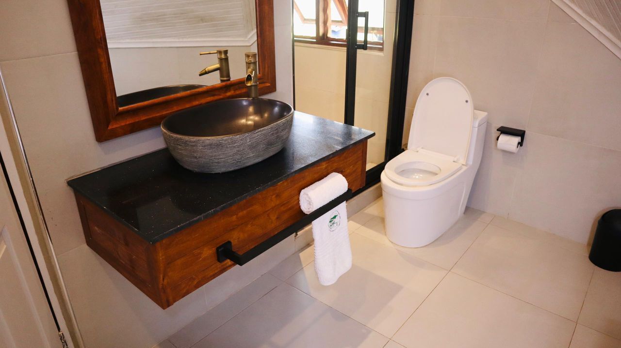 A bathroom with a wooden vanity, a large vessel sink, a white toilet, and a towel hanging on the wall.