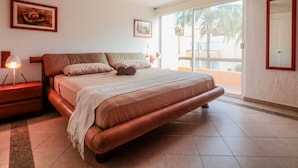 Una camera da letto con un letto grande, un comodino, una lampada e una finestra vista palme.