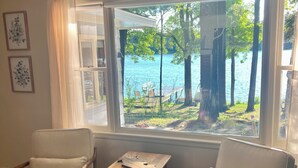 Ein Zimmer mit zwei weißen Sesseln, einem kleinen Holztisch und einem Fenster mit Blick auf einen See und Bäume.