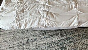 Ein Bett mit weißer Steppdecke, ein beiges Sofa und ein gemusterter Teppich.