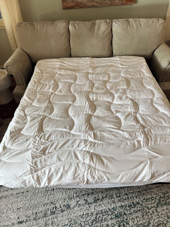 Ein Bett mit weißer Steppdecke, ein beiges Sofa und ein gemusterter Teppich.