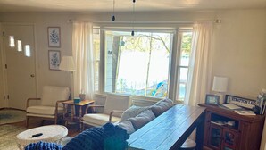 Ein geräumiges Wohnzimmer mit Deckenventilator, Esstisch, einer Couch und Blick ins Freie durch große Fenster.