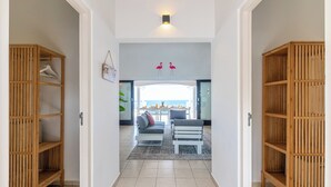 A modern living room with a sofa, two chairs, and a coffee table. There is a wooden bookshelf on the left and a wooden cabinet on the right. A sign on the wall reads "COOKING STOP HERE".