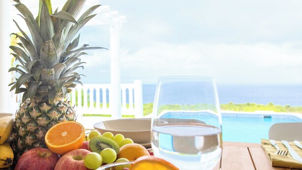 A table with fruits, a glass of water, and a view of the ocean.