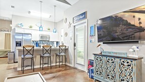 Una cocina moderna con armarios blancos, un refrigerador de acero inoxidable y un comedor con taburetes de bar.