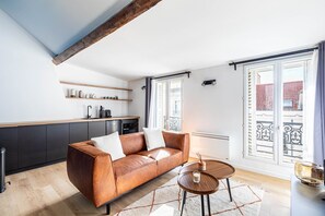 A modern living room with a brown leather sofa, a small wooden table, and a kitchen area with dark cabinets and a white countertop. - GuestReady - serene stay near Champs de Mars (Paris)