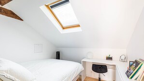 Une petite chambre à coucher moderne, dotée d’une lucarne, d’un lit, d’un bureau et d’une chaise.
