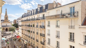 Un immeuble à plusieurs étages doté de balcons, une rue bordée de piétons et une église en arrière-plan.