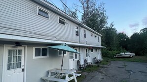 Een motel met twee verdiepingen, met een rij eenpersoonskamers, elk met een deur en raam. Voor een van de kamers staat een picknicktafel met een groene parasol.