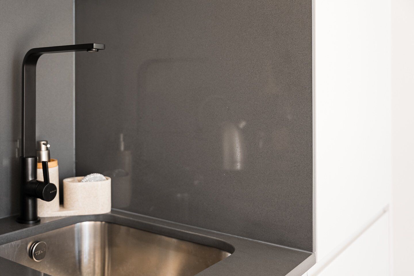 Eine moderne Küche mit Spüle aus Edelstahl, einem schwarzen Wasserhahn und einer strukturierten Spritzschutzwand.