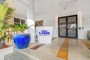 A reception area with a large blue planter, a white sign for Miss Greef Beach Bar & Grill, and a patterned wall. - Corendon Beach Plaza South Beach Miami (Miami Beach)