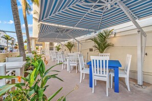 Eine Außenpatio-Terrasse mit weißen Tischen und Stühlen, einem blauen Tisch und gestreiften Sonnenschirmen.