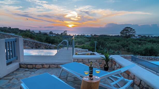 Eine Terrasse mit Pool, Liegestühlen und Blick auf den Sonnenuntergang.