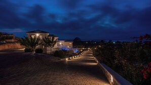 Ein gepflasterter Weg führt zu einem Haus mit Pool, umgeben von Pflanzen und blauem Himmel.