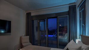 Ein Hotelzimmer mit Bett, Stuhl, Fernseher und einem Balkon mit Blick.