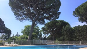 A swimming pool with a tiled deck, surrounded by a metal fence and trees. - Villa Située Dans un Domaine Prisé Avec Plage Privée + Transats ! (Grimaud)