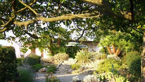 A garden with stone steps leading to a house, surrounded by various plants and trees. - Villa Située Dans un Domaine Prisé Avec Plage Privée + Transats ! (Grimaud)