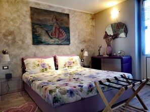 A bedroom with a bed, a nightstand, a dresser, a mirror, and a painting on the wall. - Cozy apartment with a garden terrace, near the central station and downtown (Milano)