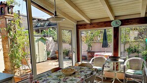 Eine überdachte Terrasse mit Tisch und Stühlen, einer Holzbalkendecke und Topfpflanzen.